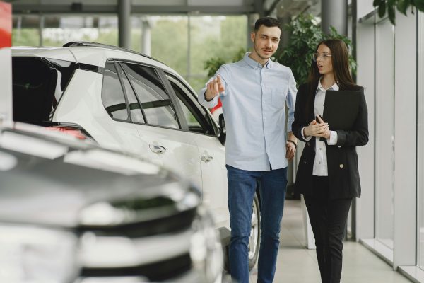 woman speaking with a potential customer who is pointing at a car in a dealership