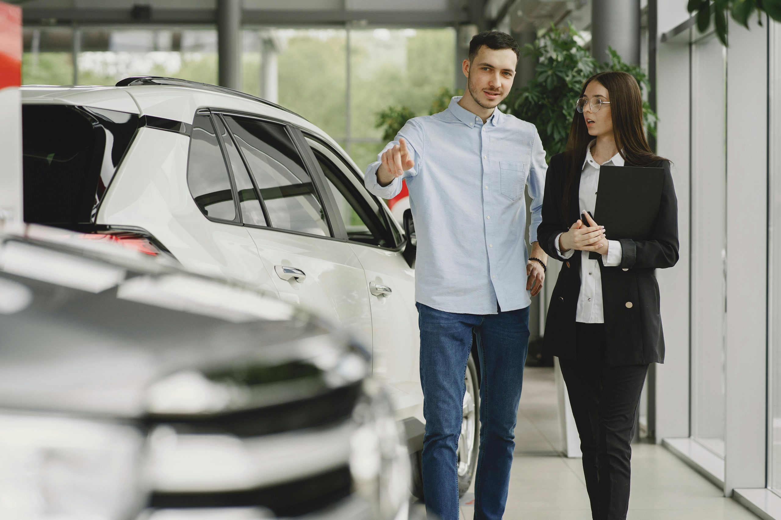 woman speaking with a potential customer who is pointing at a car in a dealership